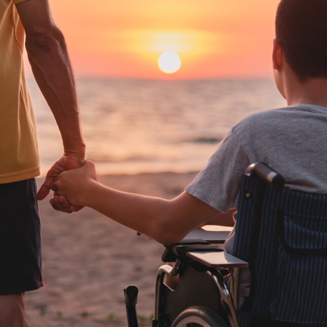 A father holds the hand of a youth sitting on a wheelchair as the two watches sunset — first opinion coverage from STAT