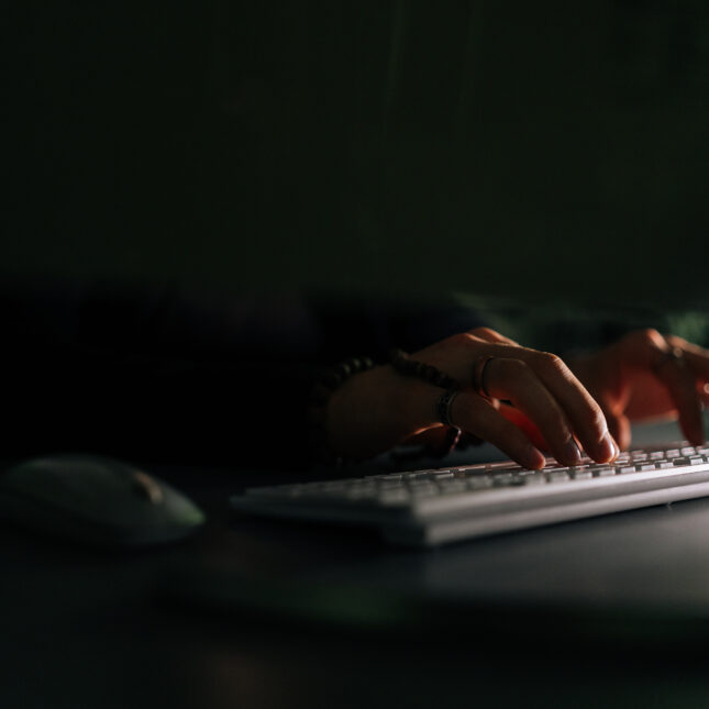 Close up stock photograph of hands typing on a keyboard, room is dark and forboding