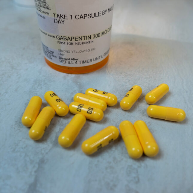 A prescription bottle for gabapentin stands behind the yellow capsules