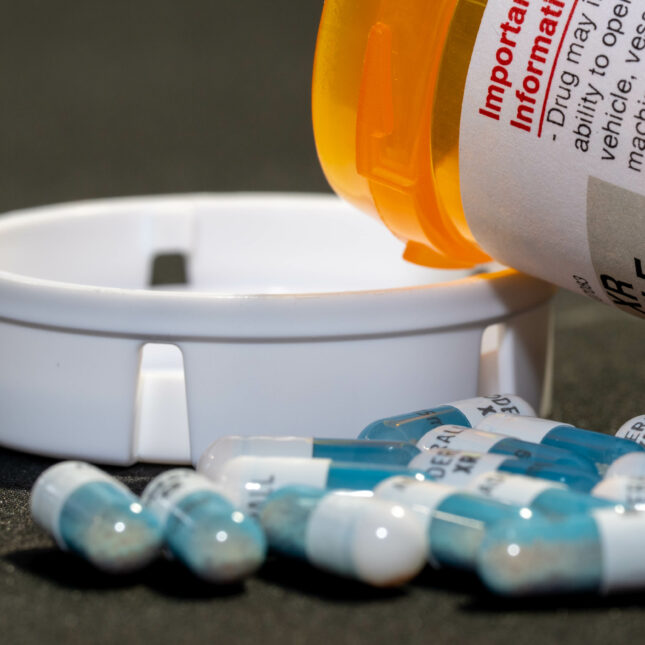 A cluster of Adderall capsules outside of an open prescription bottle that leans on its cap — health tech coverage from STAT