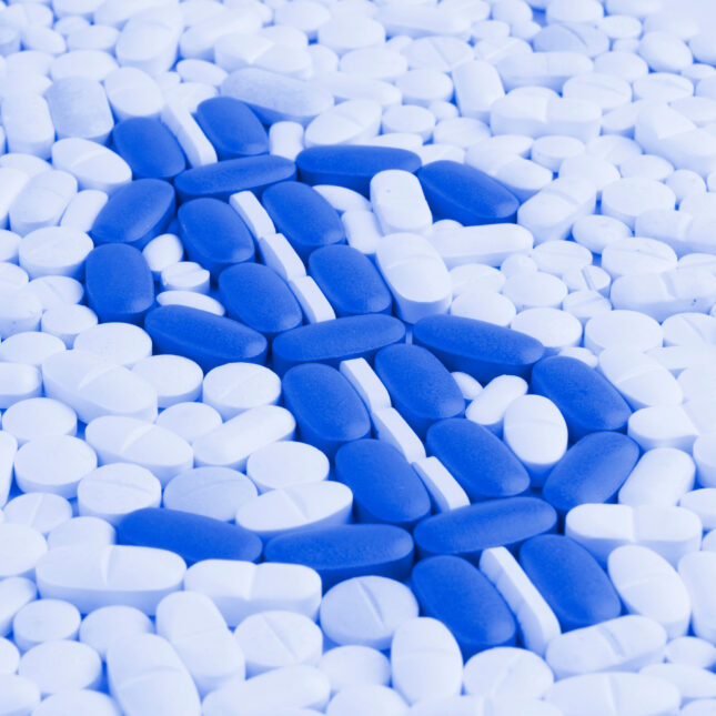 Blue pills in the shape of a dollar sign surreound by white pills. -- Health Policy coverage from STAT