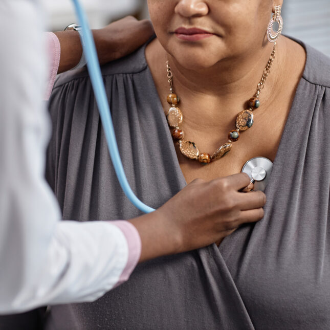 Cropped photograph of female patient at check up in clinic with doctor pressing stethoscope to her chest