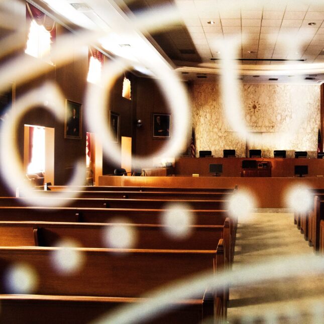 An empty courtroom viewed through a glass window labeled with the word "COURT" — first opinion coverage from STAT