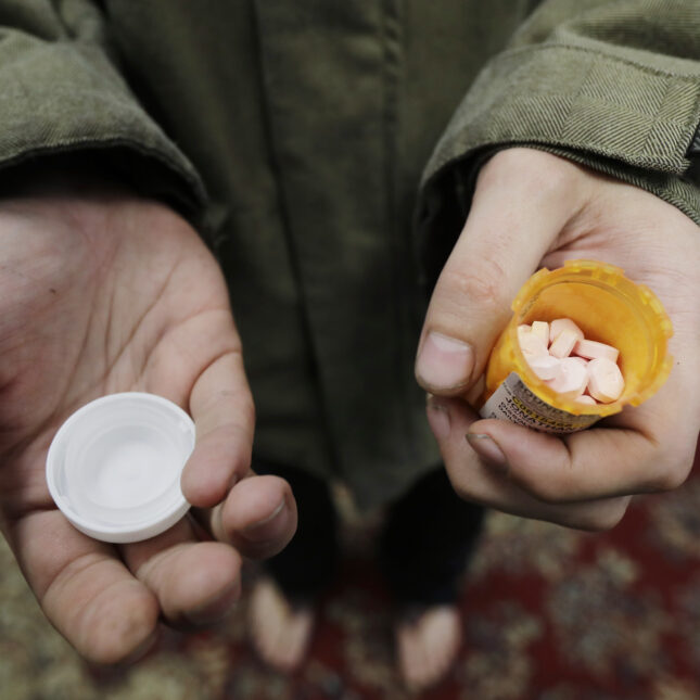 A person holds a bottle of buprenorphine on one hand and the cap on the other hand — health coverage from STAT