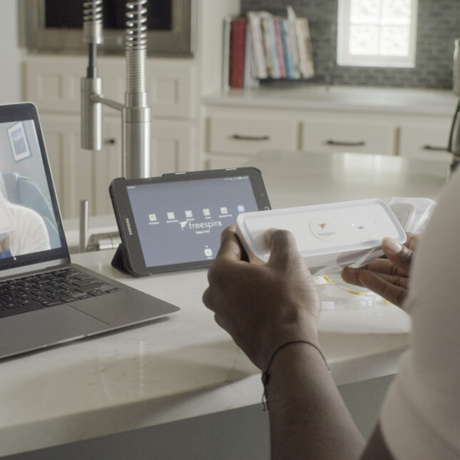 A person operates a Freespira, the only medication-free, FDA-cleared digital therapeutic treatment, sitting in front of a laptop screen showing another person holding the device — health tech coverage from STAT