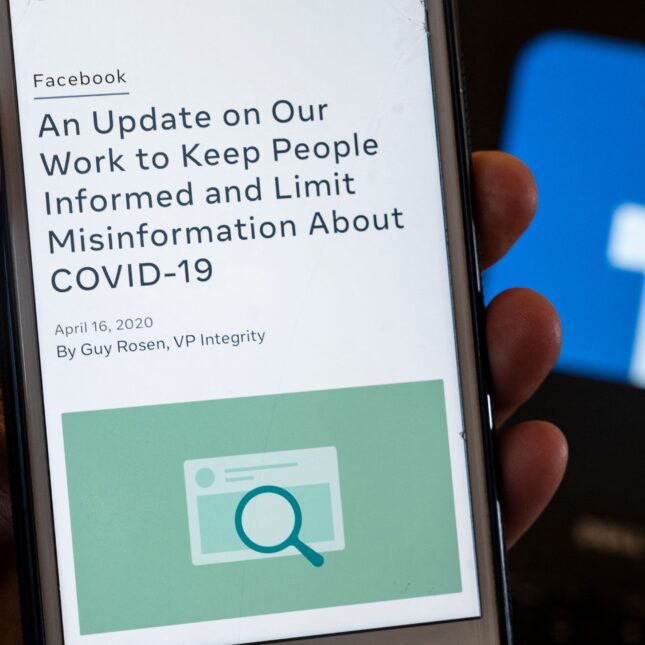 A phone screen displays Facebook's updated policy on its effort in limiting COVID-19 misinformation, in front the platform's logo — politics coverage from STAT