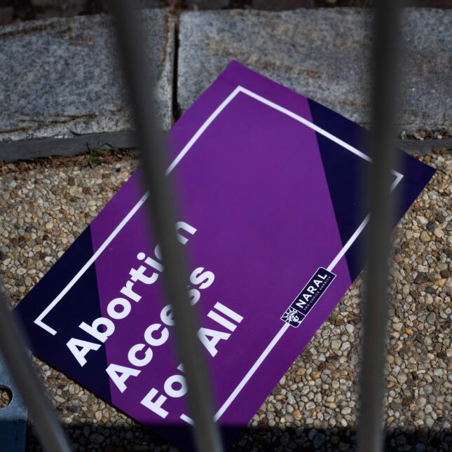 a sign reading "Abortion Access For All" lays on the ground behind a fence – first opinion coverage from STAT