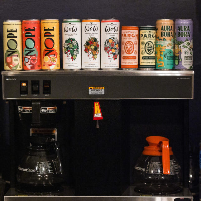 Four brands, ten cans of non-alcoholic beverages line up on top of a coffee machine at a lounge — first opinion coverage from STAT