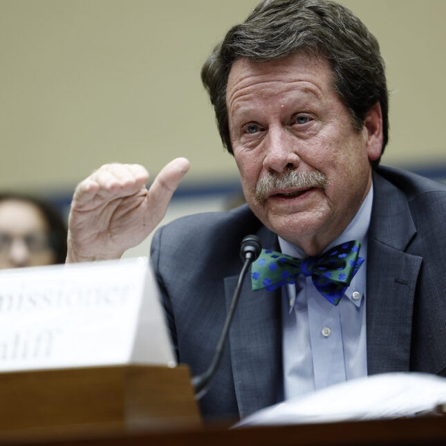 Commissioner of the FDA Dr. Robert Califf, donning a red and blue bow tie, gestures with his right hand while testifying at a hearing — politics coverage from STAT