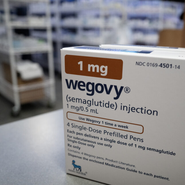 Two boxes of Wegovy, the front one covering the back one, on a table in a pharmacy— first opinion coverage from STAT