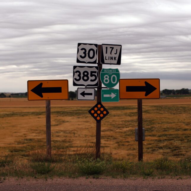 On the side of a field, a stand holding a group of four road signs stands between a sign with an arrow pointing to the left and a sign with an arrow pointing to the right — first opinion coverage from STAT