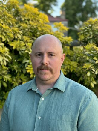 Portrait of Allen Haddrell wearing a green shirt, with yellowish/green bushes behind him. -- infectious disease coverage from STAT